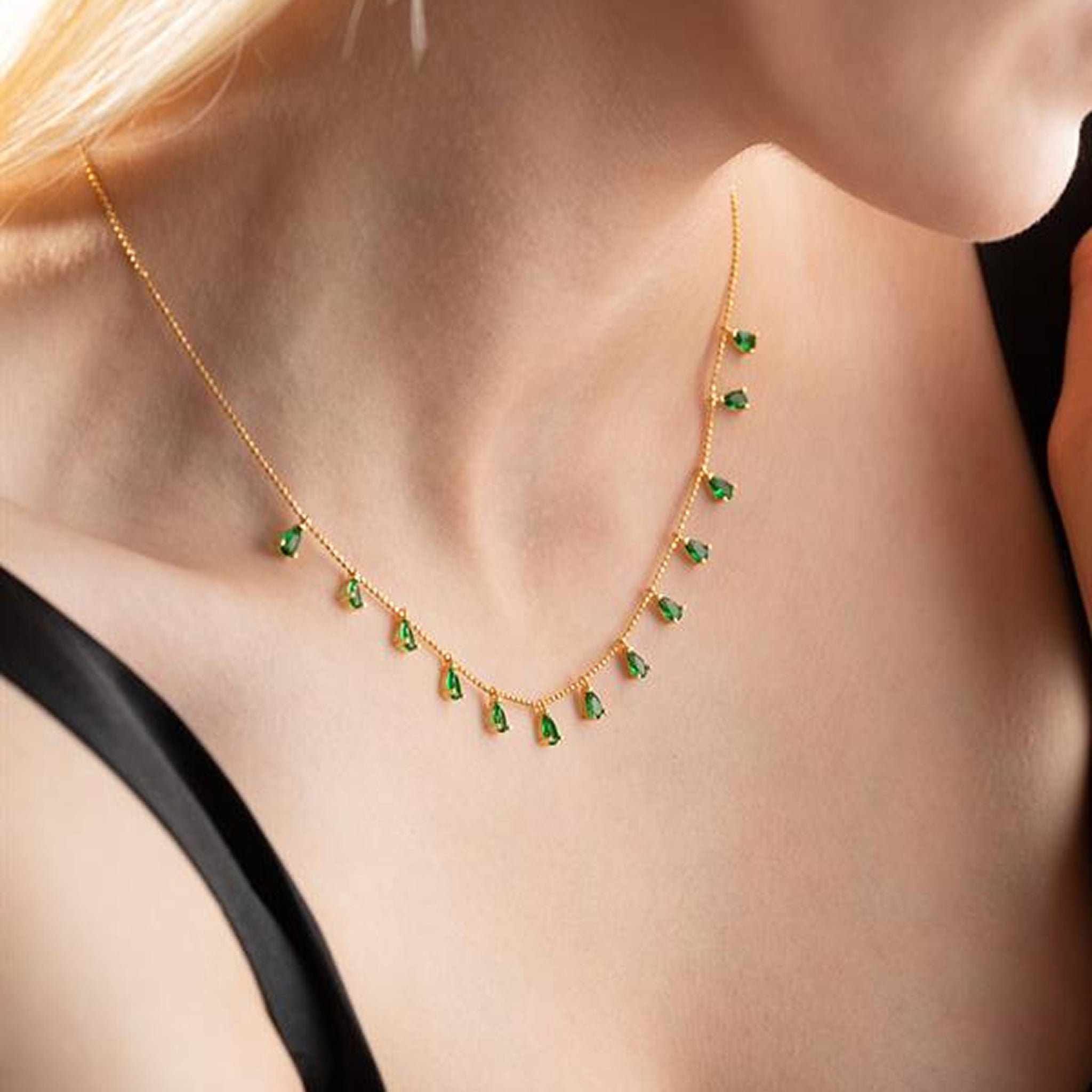 Gold necklace with green gemstones worn by a person