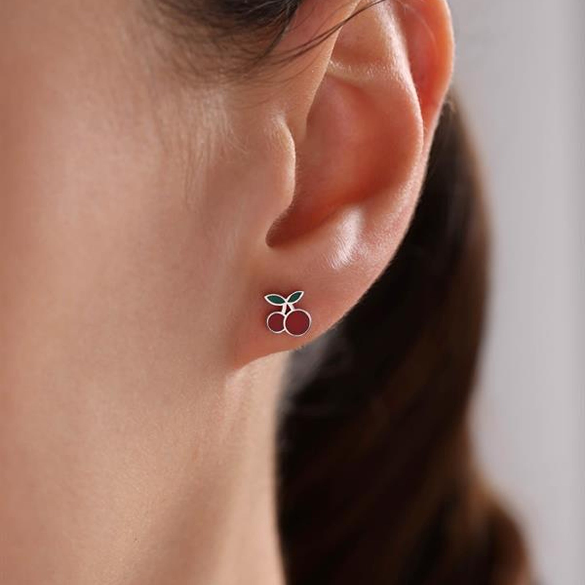 Close-up of an ear wearing a cherry stud earring with a blurred background