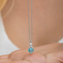 Teardrop-shaped pendant with blue gemstone on a chain, held by a person.