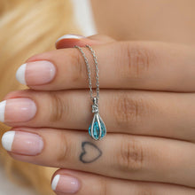 Hand wearing a silver necklace with a blue teardrop pendant