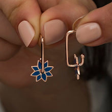 Rose gold earrings with blue floral and cactus designs held by a hand.