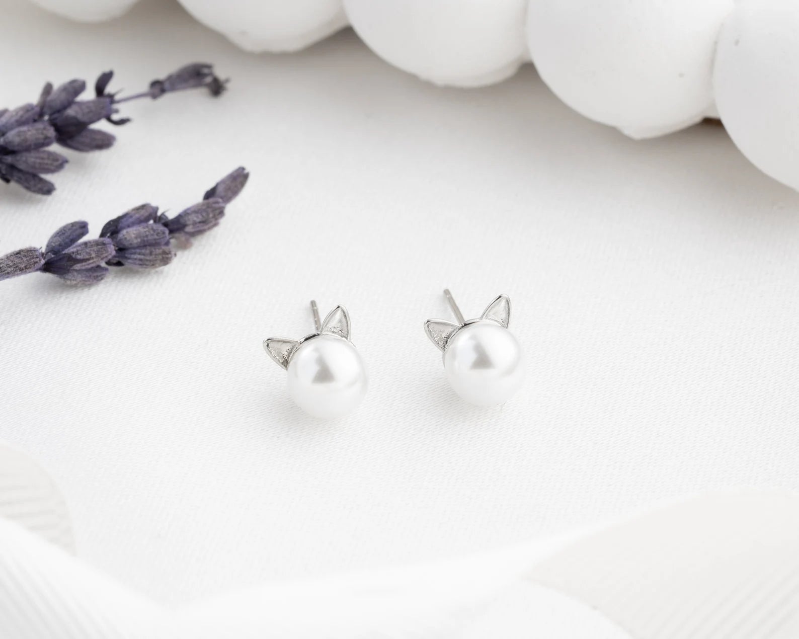Silver cat-shaped earrings on a white surface with lavender flowers.