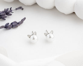 Silver cat-shaped earrings on a white surface with lavender flowers.