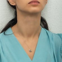 Woman wearing a blue top with a necklace featuring a moon pendant against a neutral background