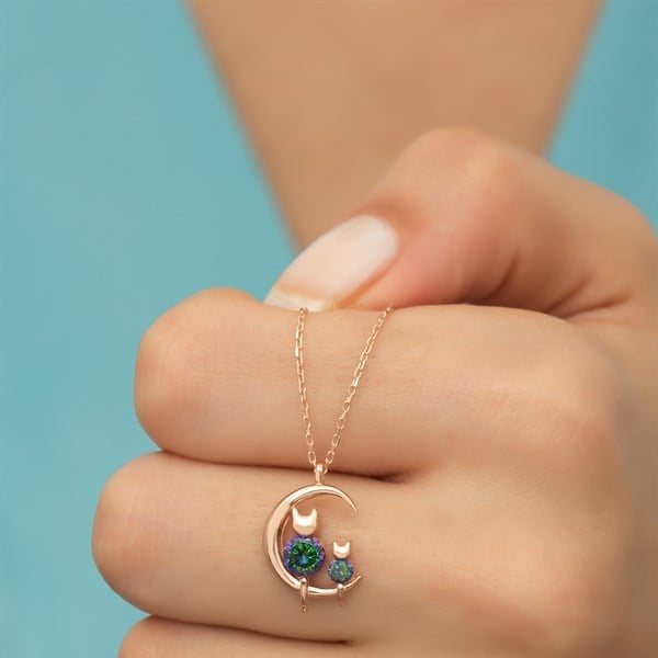Hand wearing a delicate gold necklace with a moon and cat pendant against a blue background