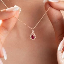 Rose gold necklace with a red gemstone held by a hand