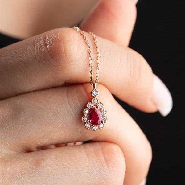 Gold necklace with a red gemstone pendant held by a hand against a black background