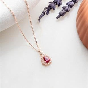 Rose gold necklace with a red gemstone pendant on a white surface.