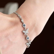 Silver bracelet with floral designs on a wrist against a neutral background