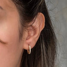 Close-up of an ear wearing a gold hoop earring with a neutral background