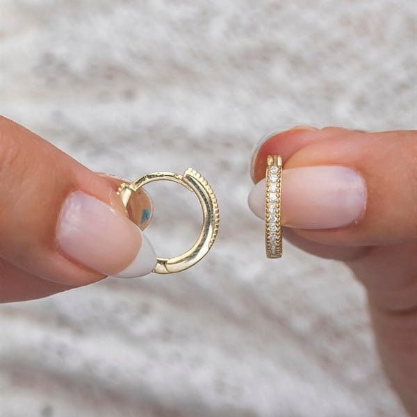 Gold hoop earrings held between fingers against a neutral background