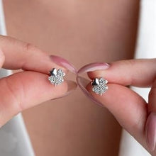 Silver flower-shaped earrings being held between fingers against a neutral background