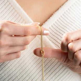 Close-up of hands holding a gold earring against a white background