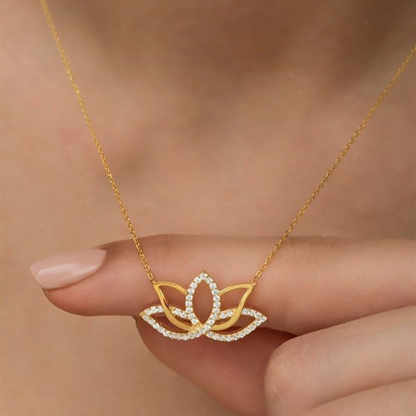 Gold necklace with a diamond-encrusted lotus flower pendant held by a hand against a neutral background