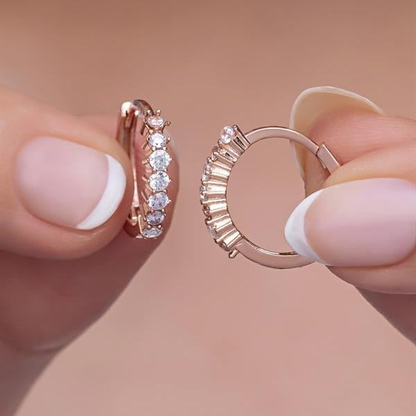 Rose gold hoop earrings held between fingers against a neutral background