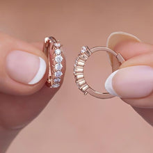 Rose gold hoop earrings held between fingers against a neutral background