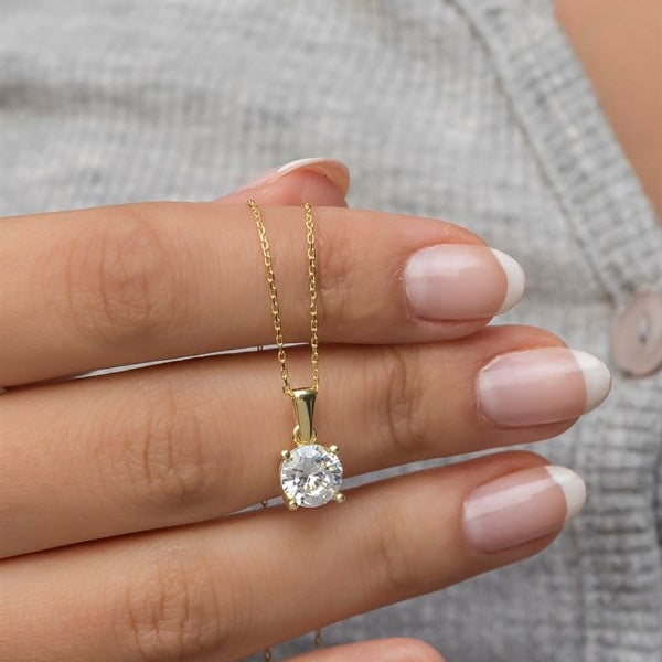 Gold necklace with a diamond pendant held by a hand against a neutral background