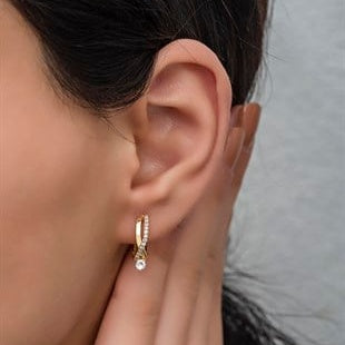 Close-up of an ear wearing a gold hoop earring with a pearl.