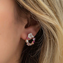 Close-up of an ear wearing a floral earring with pearls and gemstones.
