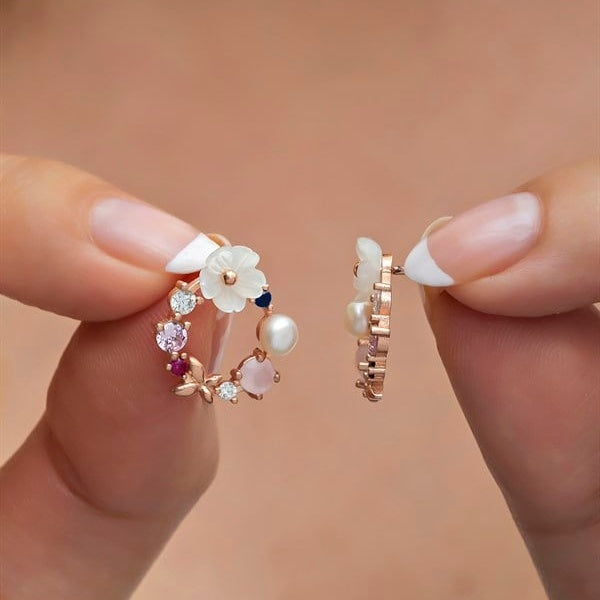Hand holding a pair of floral earrings with gemstones against a beige background