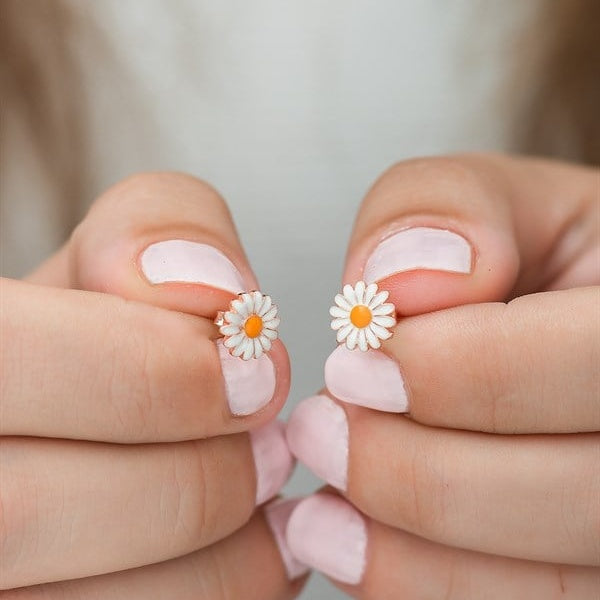 Flower-shaped earrings held between two fingers with a neutral background