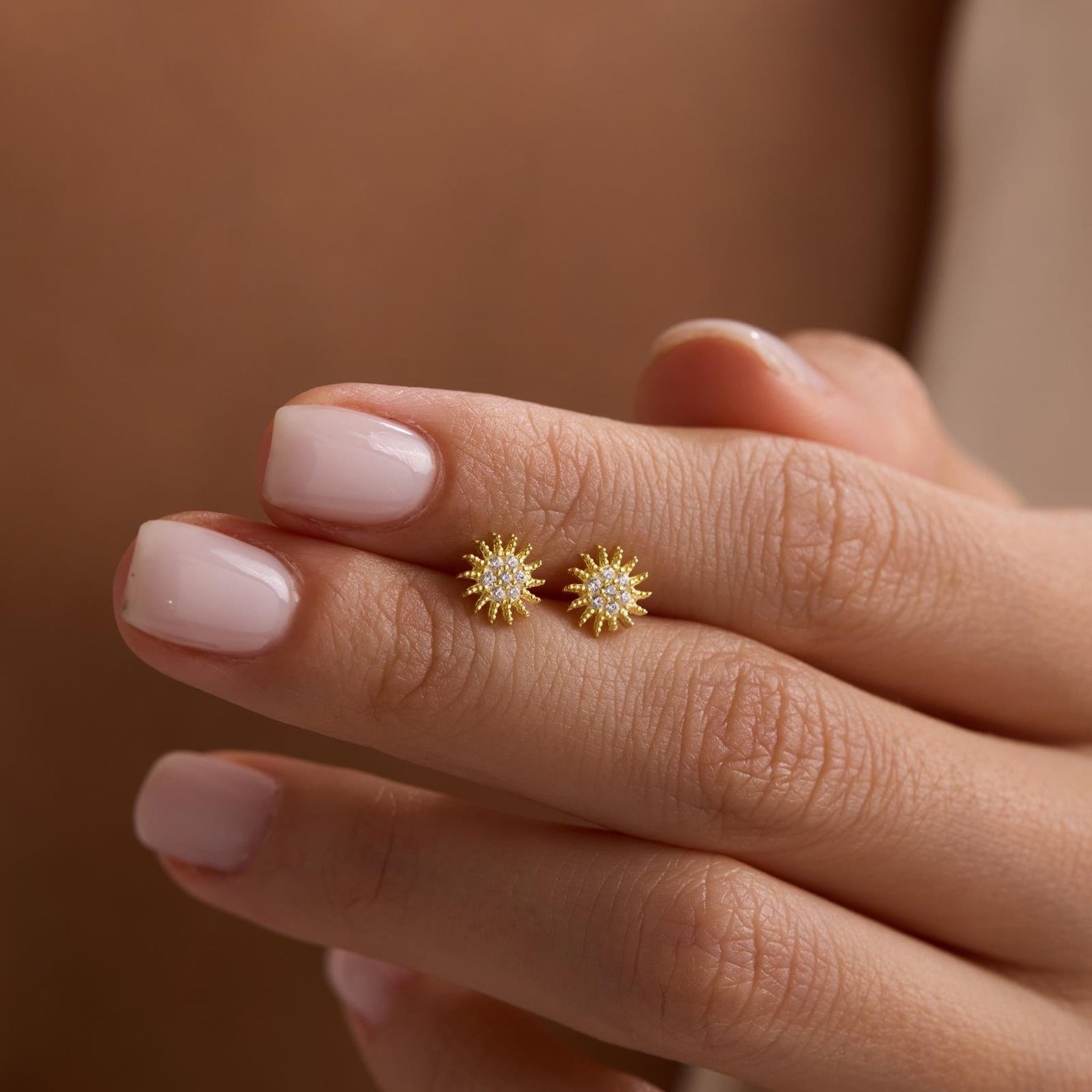 Gold sunflower earrings on a hand with a blurred background