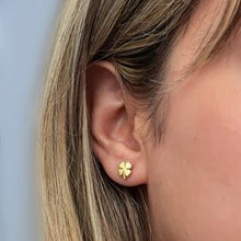 Gold four-leaf clover earring worn by a person with blonde hair.