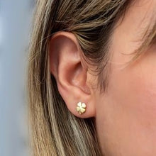 Gold four-leaf clover earring worn by a person with blonde hair.