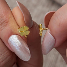 Gold four-leaf clover earrings held between fingers with a neutral background