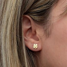 Gold four-leaf clover earring worn by a person with blonde hair.