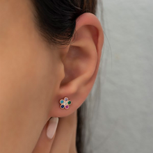 Close-up of an ear wearing a colorful floral earring with a neutral background