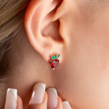 Close-up of an ear wearing a heart-shaped earring with green leaves.