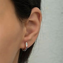 Close-up of an ear wearing a silver earring with a gray background