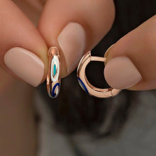 Rose gold hoop earrings with colorful accents held between fingers against a blurred background