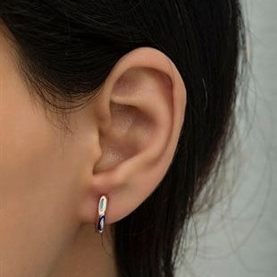 Close-up of an ear wearing a small hoop earring with dark hair and blurred background