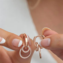 Rose gold hoop earrings with small diamonds held between fingers against a neutral background