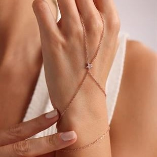 Close-up of a hand wearing a delicate bracelet with a pink gemstone on a neutral background