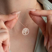 Person wearing a silver necklace with a tree pendant on a plain background
