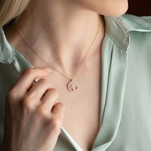 Necklace with a circular pendant worn by a person in a light green shirt.