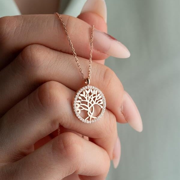 Rose gold necklace with a tree of life pendant held by a hand against a neutral background