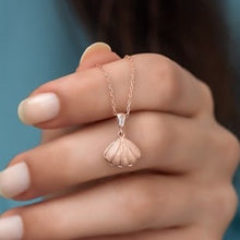 Rose gold shell pendant necklace on a hand against a blue background