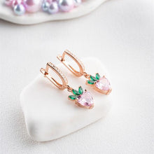 Rose gold earrings with pink gemstones and green leaves on a white heart-shaped stand.