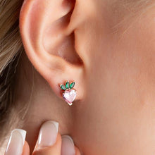 Close-up of an ear wearing a stud earring with green and pink gemstones.