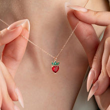 Necklace with a strawberry pendant held by hands against a neutral background