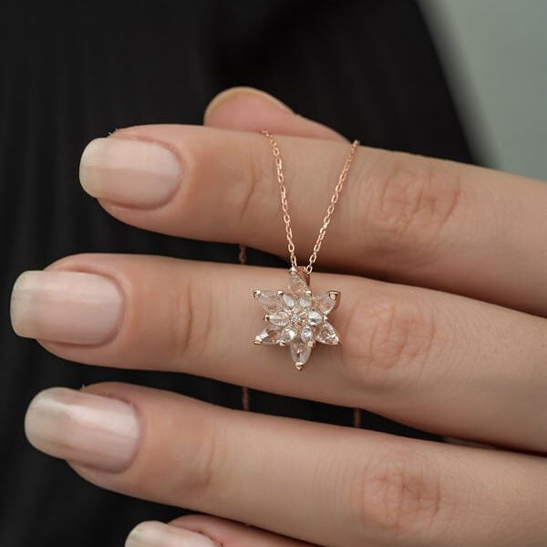 Rose gold necklace with a star-shaped pendant held by a hand against a dark background