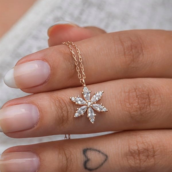 Rose gold snowflake pendant necklace on a finger with a blurred background