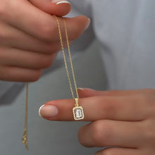 Gold necklace with a diamond pendant held by a hand against a neutral background
