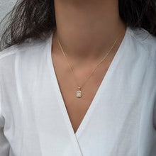 Necklace with a square pendant worn by a person in a white shirt
