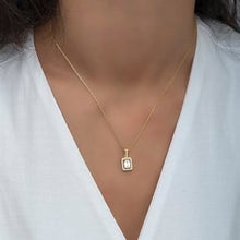Gold necklace with a square pendant worn by a person in a white top