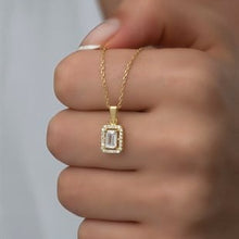 Gold necklace with a diamond pendant held by a hand against a neutral background